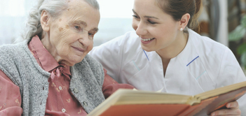 older woman with young female caregiver reading a book older woman with young female caregiver reading a book